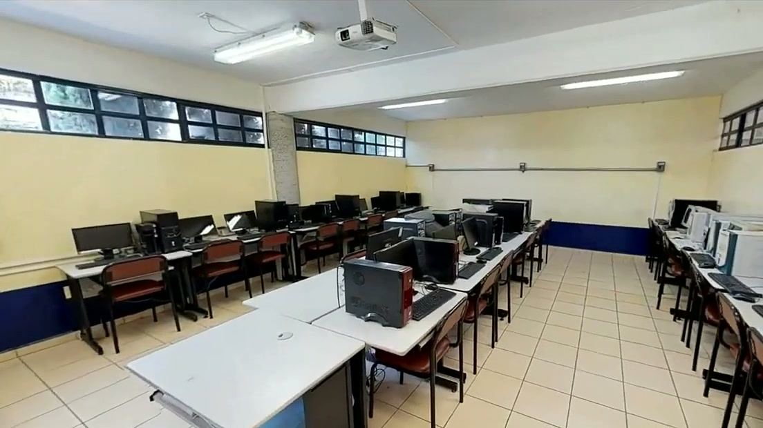 Aula de cómputo con varias filas de computadoras de escritorio sobre mesas.