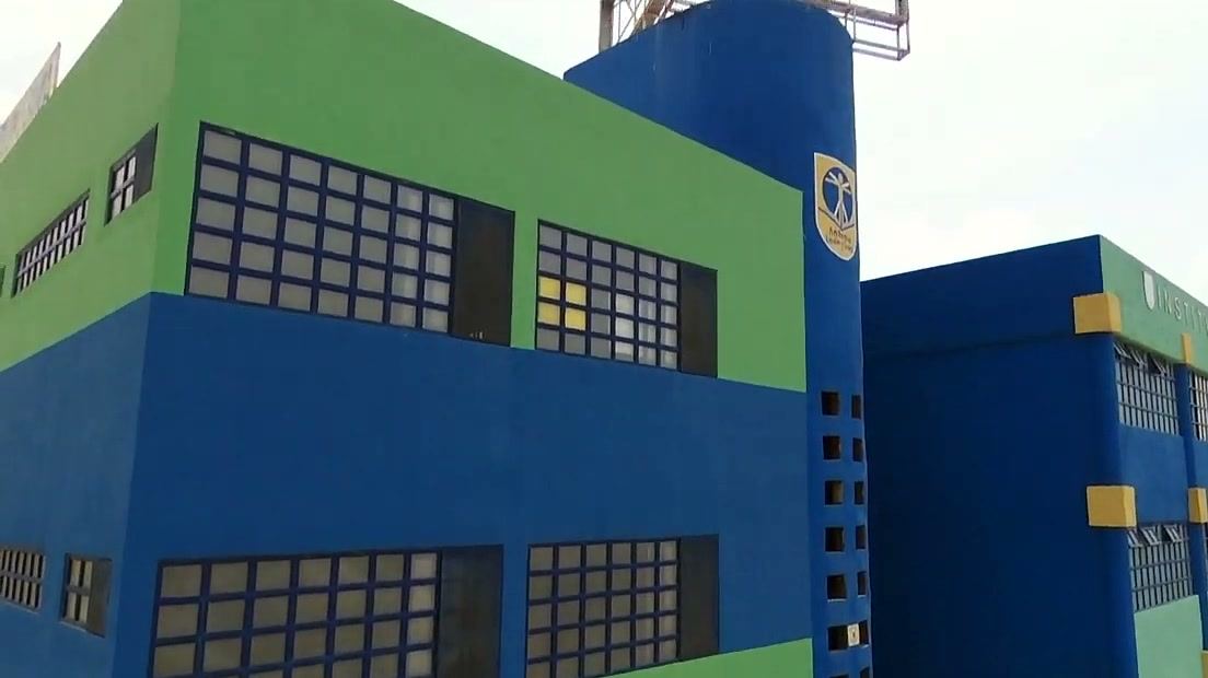 Esquina del edificio en azul y verde con una torre que muestra el emblema del instituto.