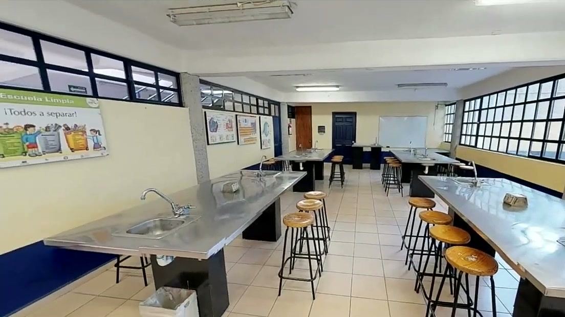 Salón con mesas largas de acero inoxidable con tarjas y bancos altos de madera.
